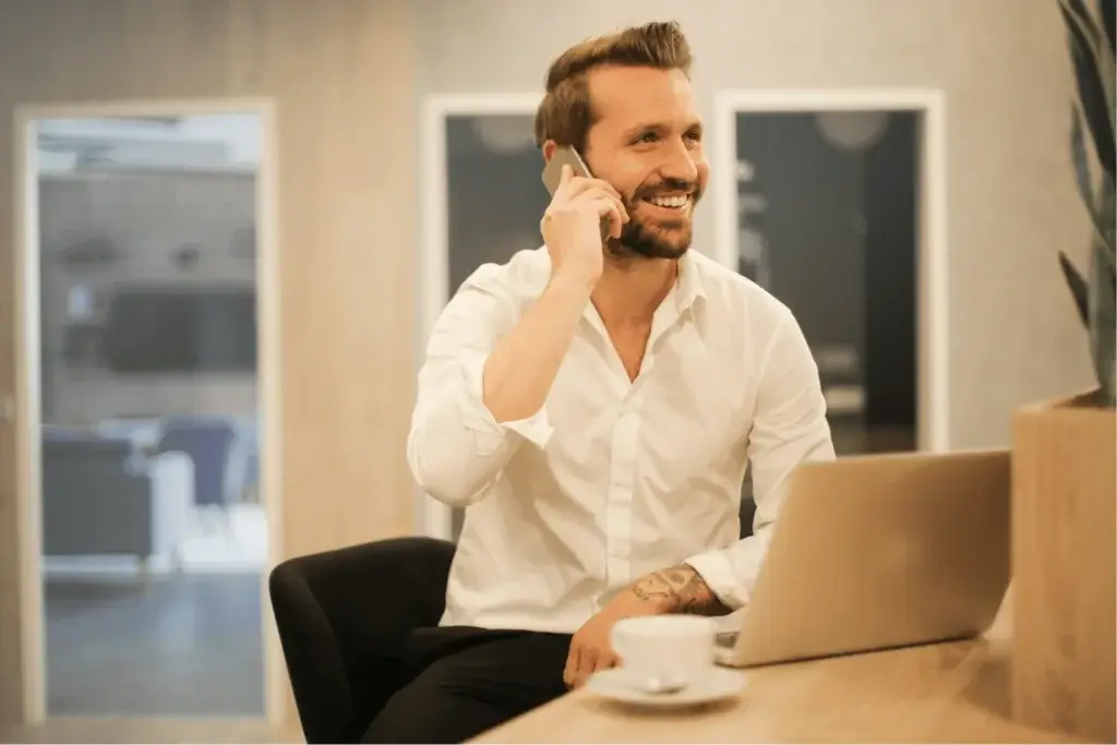 business owner on the phone at a counter with a laptop open next to a cup of cup of coffee
