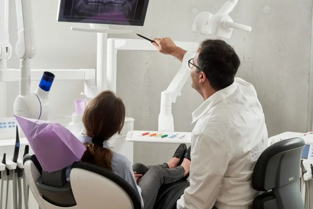 A patient and dentist reviewing x-rays on a monitor above them.