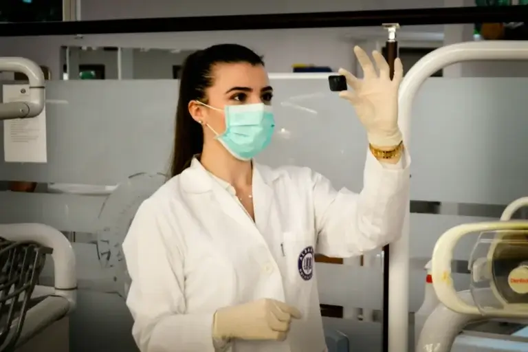 Dental professional in a clinical setting reviewing a dental X-ray or imaging sensor while wearing protective gloves and a face mask.